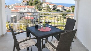 Un balcon avec une table et des chaises, donnant sur une ville côtière avec ses maisons et un ciel dégagé.