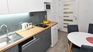 Une cuisine moderne avec des armoires blanches, un plan de travail en bois, une cuisinière, un four à micro-ondes et un lave-vaisselle. On y trouve une table à manger avec des chaises et une porte dotée de poignées dorées.