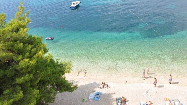 Une plage avec une eau turquoise et limpide, un bateau et des gens qui se détendent sur le sable.