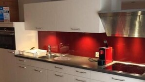 A modern kitchen with white cabinets, a stainless steel range hood, and a red backsplash. - CasaMarmarolla by Interhome (Breil/Brigels)