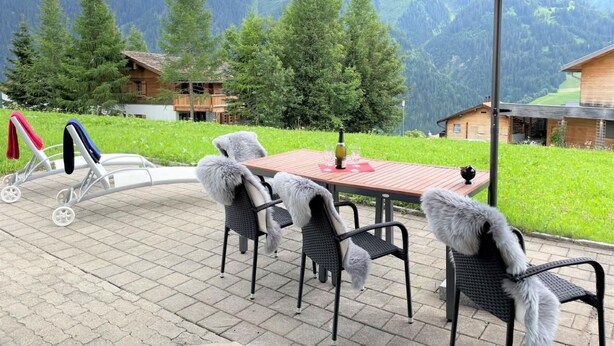 Une terrasse extérieure avec une table et des chaises, un parasol rouge et une vue panoramique sur les montagnes.