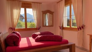 Une chambre avec un lit en bois, deux fenêtres avec des rideaux, un miroir et une vue sur les montagnes.