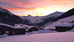Un village de montagne enneigé, avec des chalets en bois et un coucher de soleil en arrière-plan.