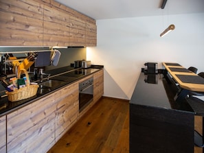 A modern kitchen with wooden cabinetry, a black countertop, and a built-in oven. - Exklusive Ferienwohnung im Hotel mit Wellness by Interhome (Laax)