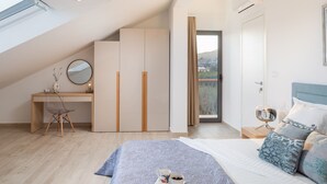 Un dormitorio moderno con techo inclinado, un escritorio con silla, una cama con cabecera azul y vistas al exterior.