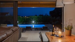 Un espacio exterior moderno con piscina, una mesa de madera con una vela y una planta en maceta.