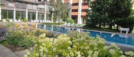 A hotel with a swimming pool surrounded by lush greenery and lounge chairs.