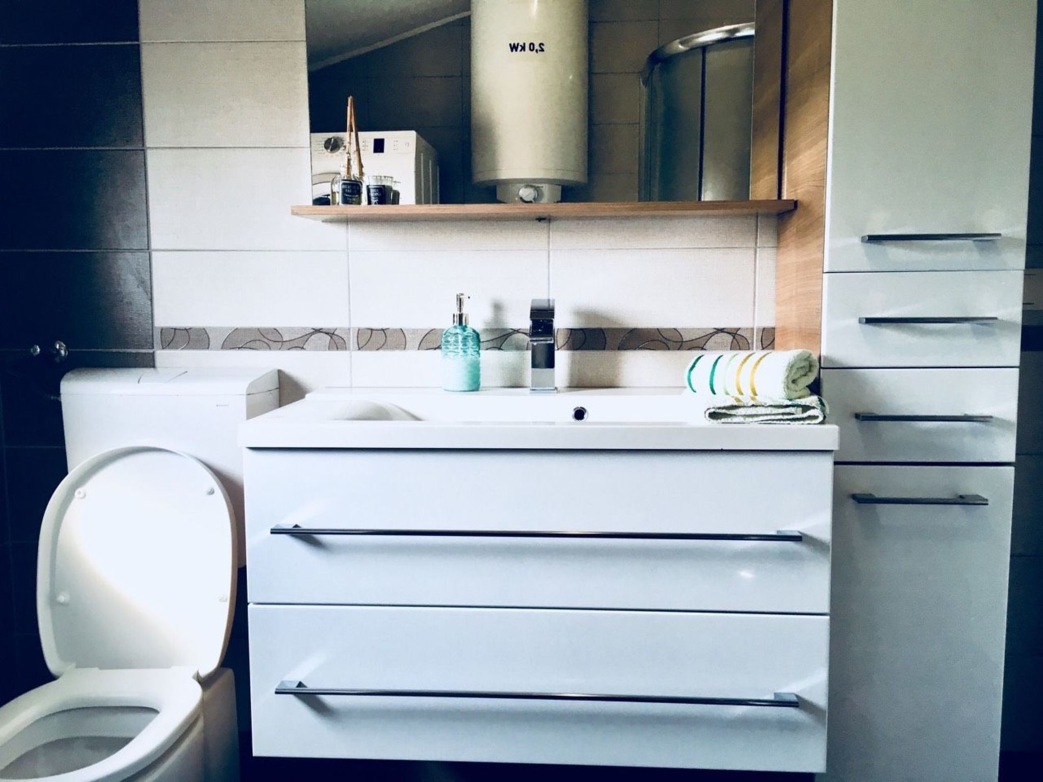 A modern bathroom with a white toilet, a sink with a mirror above, and a towel rack with folded towels.