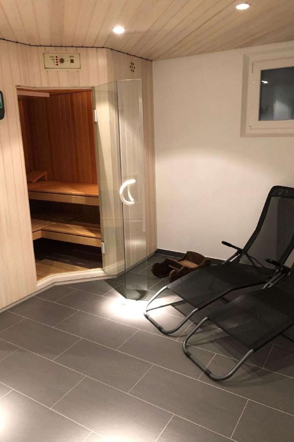 A sauna room with a glass door, a wooden bench, and a black chair.