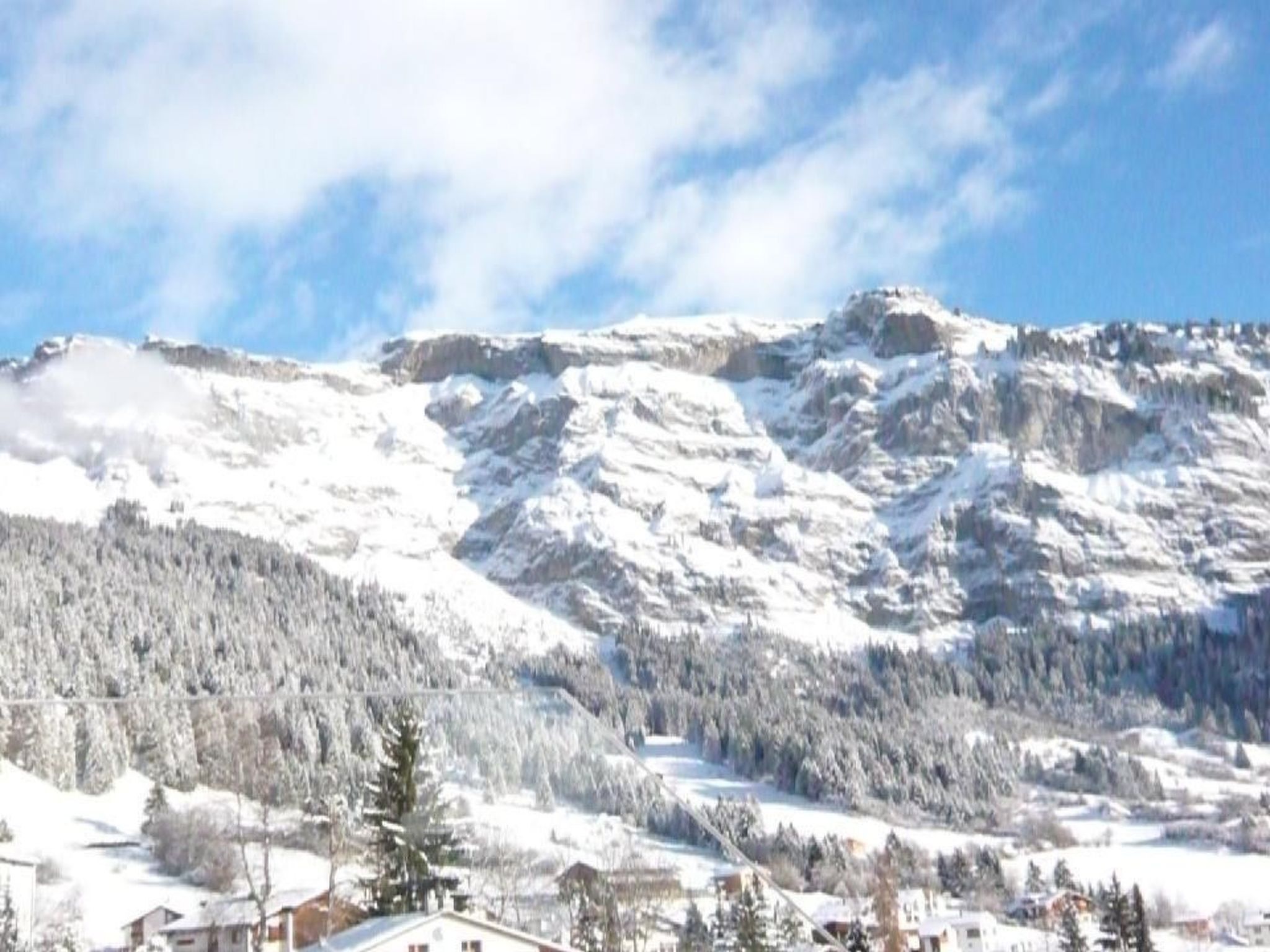 A snow-covered mountain with a forested valley and buildings at the base.