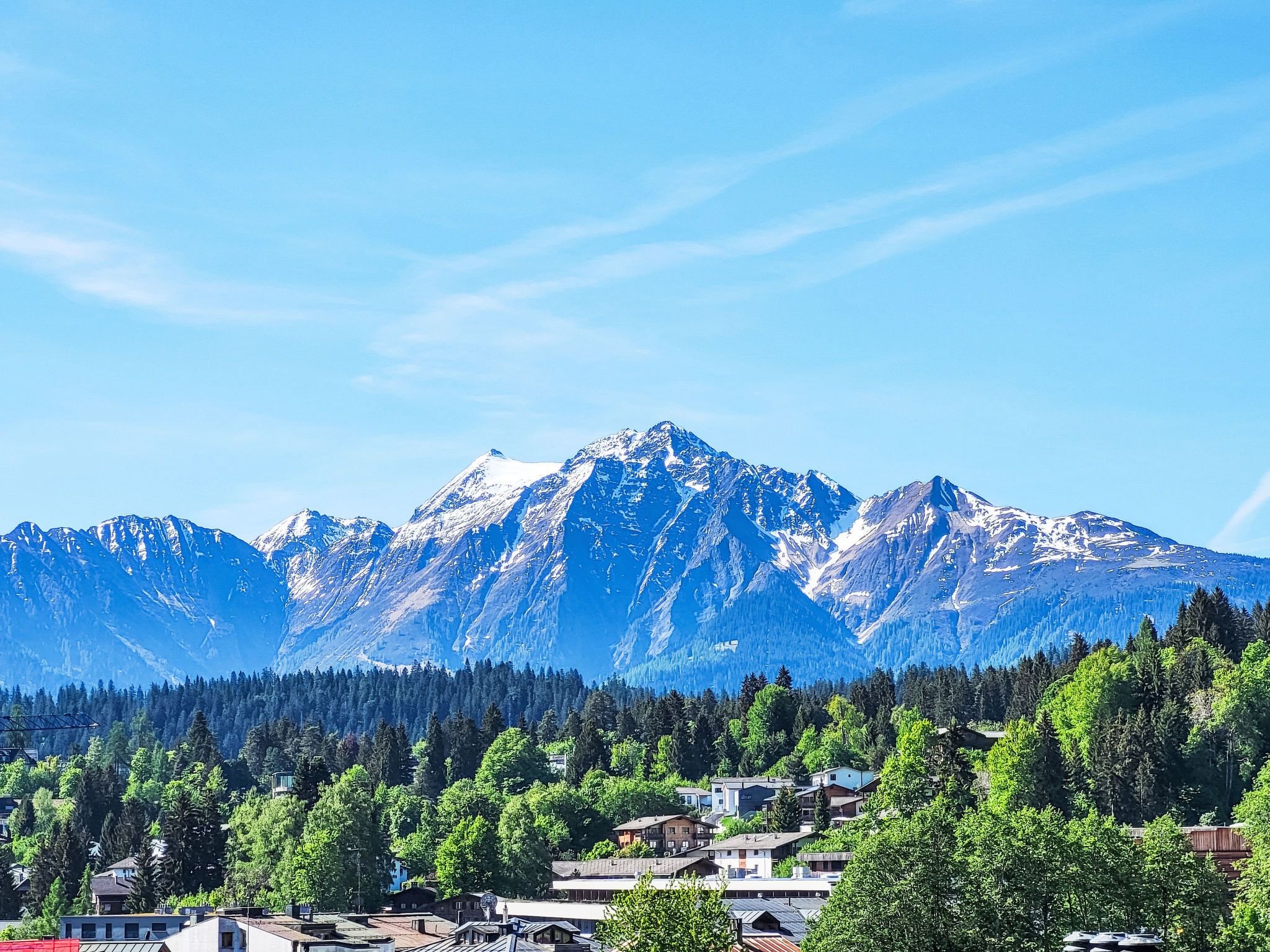 A mountain range with snow-capped peaks, a forested valley, and a small town with buildings.