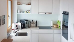 Una cucina compatta con mobili bianchi, forno integrato e soffitto in legno.