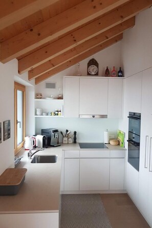 Een kleine keuken met witte kastjes, een inbouwoven en een houten plafond.