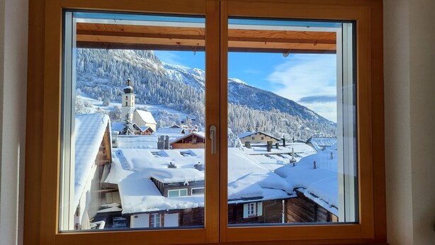 Una stanza con un'ampia finestra in legno che si affaccia su un villaggio innevato, con case e una chiesa.