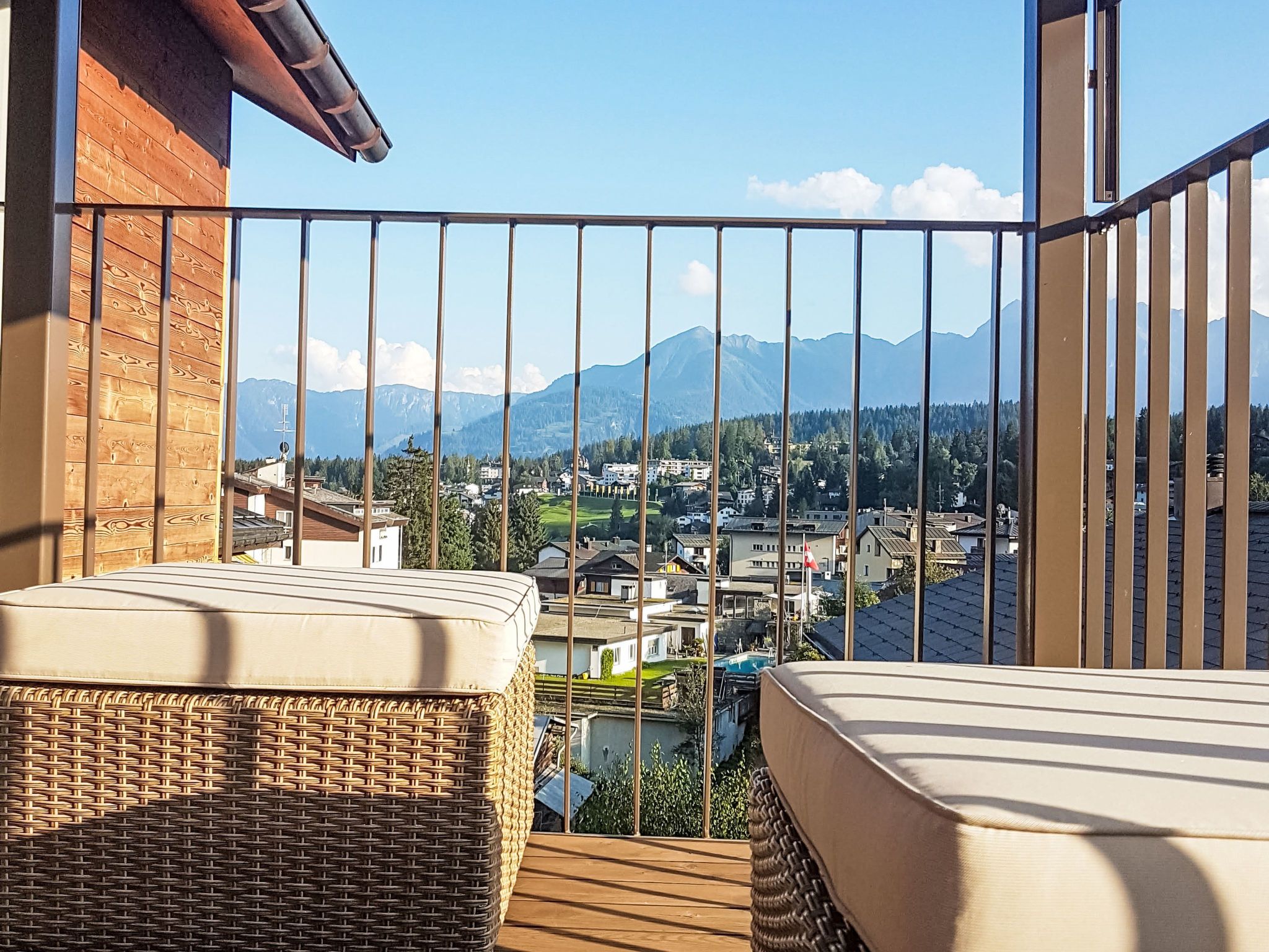 Ein Balkon mit Korbmöbeln und Blick auf eine Stadt und Berge.