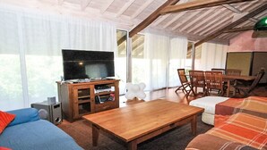 Una sala de estar acogedora con televisor, muebles de madera y ventanas amplias.