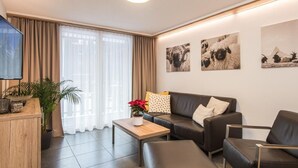 A modern living room with a sofa, armchairs, a coffee table, and a TV. There are three framed pictures on the wall and a window with curtains. - Top Ferienwohnung Pollux für 4-5 Personen by Interhome (Zermatt)
