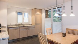 A modern kitchen with granite countertops, wooden cabinets, and a dining area with a wooden table and chairs. - Top Ferienwohnung Pollux für 4-5 Personen by Interhome (Zermatt)
