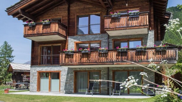 Eine mehrstöckige Holzhütte mit Balkonen, Steinverzierungen und Außenmöbeln.
