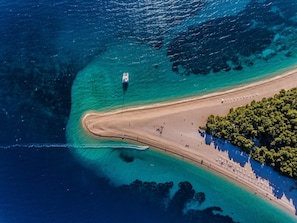 An aerial view of a beach with clear turquoise waters, a boat, and a densely vegetated area. - "Blue Apartment" am Strand by Interhome (Brač/Bol)