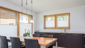 A modern kitchen with dark cabinets, a wooden dining table, and black chairs. There are two windows with blinds, and a hanging light fixture above the table. - Top Ferienwohnung Monte Rosa (SkiIn/SkiOut) by Interhome (Zermatt)