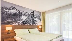 A modern hotel room with a large bed, wooden headboard, two bedside lamps, and a mountain landscape mural on the wall. - Top Ferienwohnung Monte Rosa (SkiIn/SkiOut) by Interhome (Zermatt)