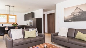 A modern living room with two sofas, a coffee table, and a dining area with a kitchen in the background. - Top Ferienwohnung Monte Rosa (SkiIn/SkiOut) by Interhome (Zermatt)