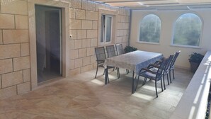 Ein überdachter Patio-Bereich mit Tisch und Stühlen, einer Tür und zwei Fenstern.