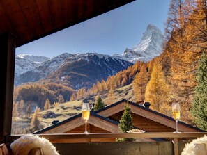 Un chalet avec vue sur la montagne, deux verres de vin sur une table et un sommet enneigé en arrière-plan.