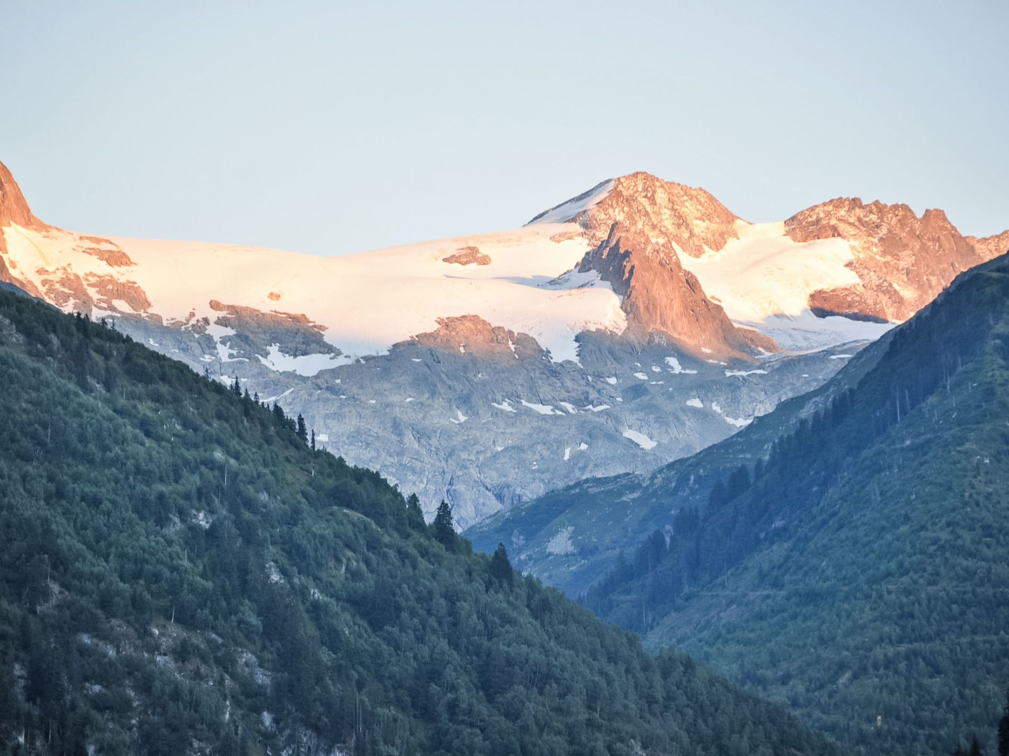 Un paysage montagneux caractérisé par des sommets enneigés et des vallées boisées et luxuriantes.