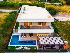 Una moderna casa a due piani con piscina sul tetto, area relax esterna e giardino curato.