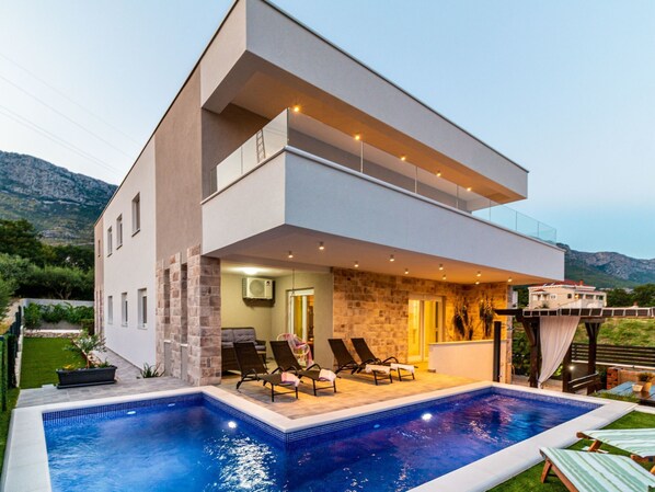Una moderna casa a due piani con piscina, area salotto esterna e vista sulle montagne.