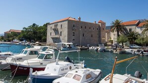 Un port de plaisance avec des bateaux amarrés, un bâtiment en pierre avec un toit rouge et des palmiers.