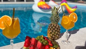 Une scène au bord de la piscine, avec un plateau de fruits, deux boissons et, au fond, des bouées en forme de licorne gonflable.