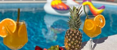 A poolside setting with a fruit platter, two drinks, and inflatable unicorn floats in the background.