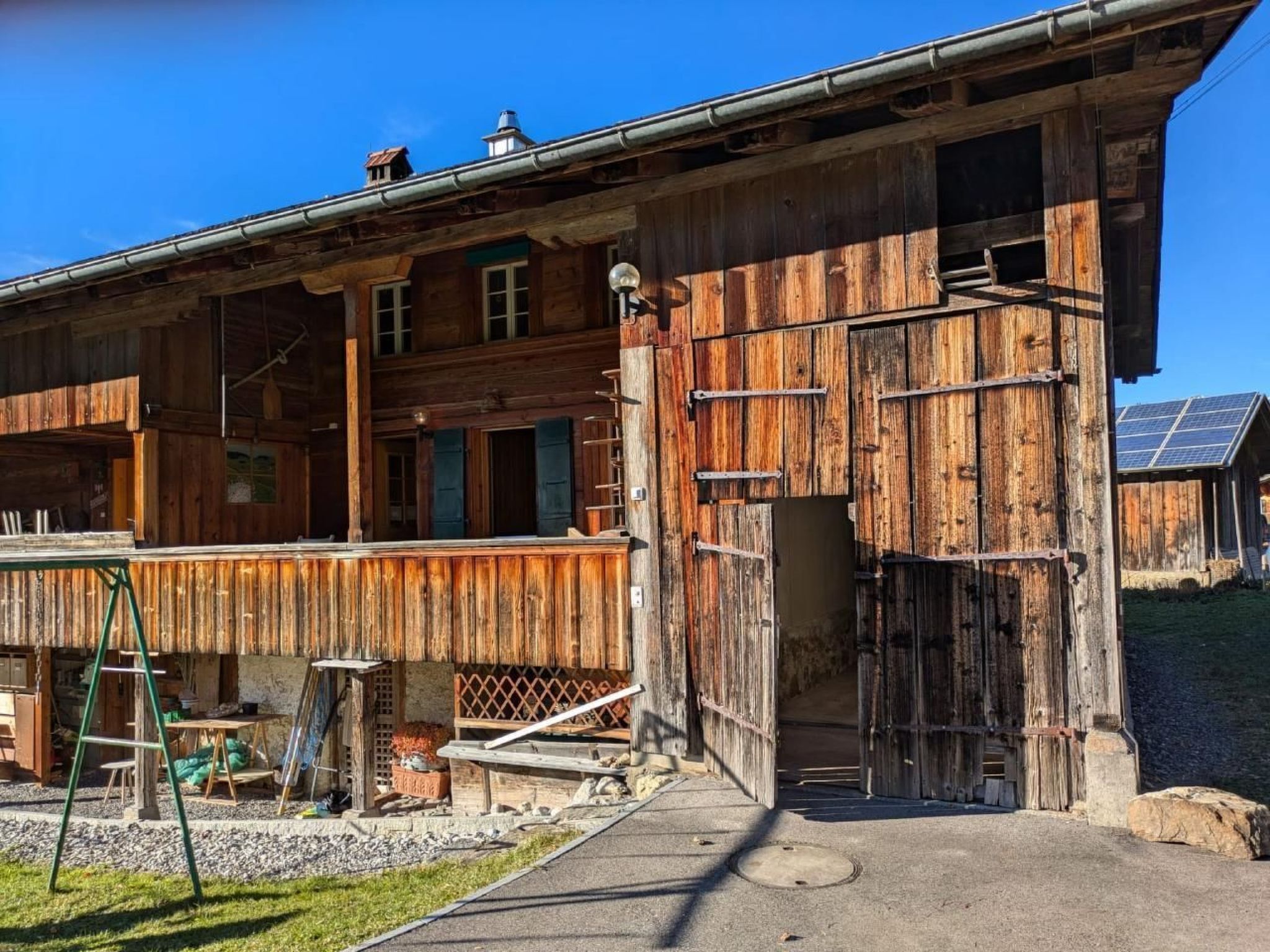 A rustic wooden building with a balcony, a ladder, and solar panels in the background.