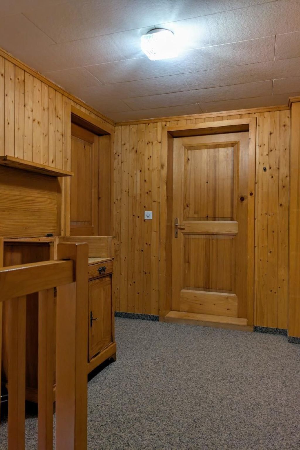 Quarto com painéis de madeira, uma porta, um banco e piso coberto por carpete.