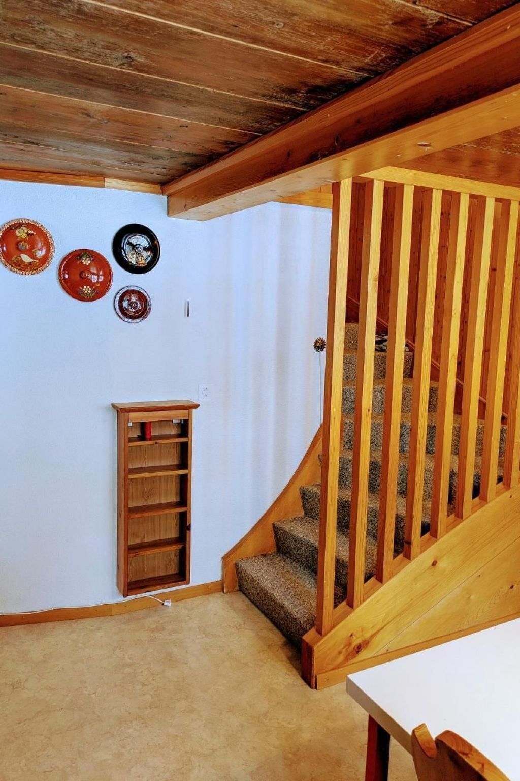 A wooden staircase with a railing, carpeted steps, and a small wooden cabinet against a white wall.