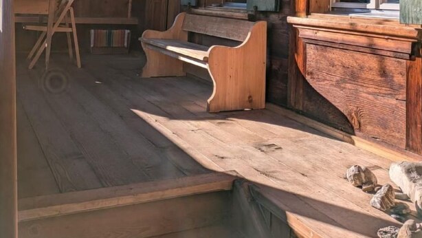 Una habitación rústica de madera con un banco, un escritorio y una ventana con contraventanas.