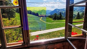 A window with a view of a green valley, a road, and a mountain range. - Ferienwohnung mit Bergpanorama by Interhome (Zweisimmen)