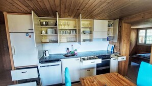 A compact kitchen with white cabinets, a stove, and a dining area with a wooden table and blue chairs. - Ferienwohnung mit Bergpanorama by Interhome (Zweisimmen)