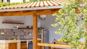 Een buitenkeuken met een houten pergola, een ingebouwde oven en een betegelde achterwand.