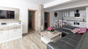 Een moderne woonkamer met een flatscreen televisie, een bank, een salontafel en een eethoek met stoelen en een tafel.