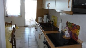 A kitchen with white cabinets, a stove, a sink, and a dining area with a chair and table. - Ferienwohnung by Interhome (Korčula/Zavalatica)