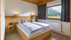 A bedroom with a wooden bed, two bedside tables, a nightstand, a window with curtains, and a view of mountains. - Appartement "Hochgefühl" by Interhome (Leutasch)