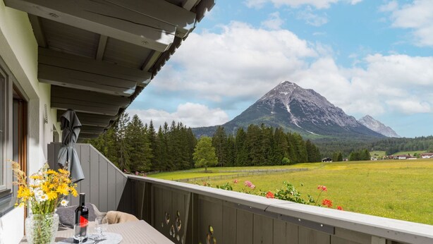 A balcony with a table set for dining, a vase with flowers, and a mountain view. - Appartement "Hochgefühl" by Interhome (Leutasch)
