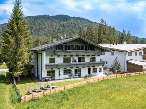 A two-story chalet with a balcony, a patio with outdoor seating, and a view of a forested mountain. - Appartement "Hochgefühl" by Interhome (Leutasch)