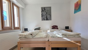 A room with two beds, a window, a painting, and a desk with a chair. - Gentiana Haus B by Interhome (Grächen)