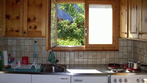 Eine Küche mit Holzausstattung, einem Fenster mit Blick ins Grüne, einer Spüle und einem Herd.