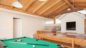 Una mesa de billar con bolas, un banco de madera y una zona de cocina con un lavabo y una ventana.